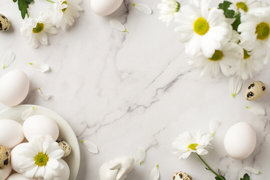 Top view photo of easter decorations bouquet of chrysanthemum flowers petals ceramic easter bunny and plate with eggs on isolated white marble texture background with empty space in the middle