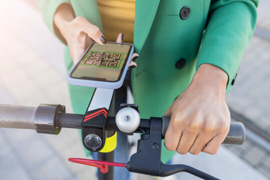 Businesswoman scanning QR code through smart phone on electric push scooter