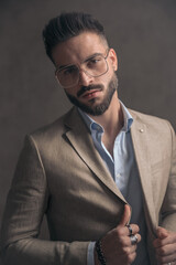 sexy businessman in beige suit with eyeglasses pulling jacket