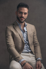 confident unshaved man with eyeglasses in beige suit sitting