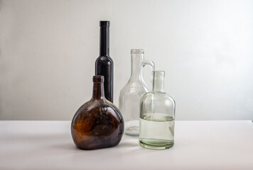 Glass bottles of different shapes and colors against a light plastered wall