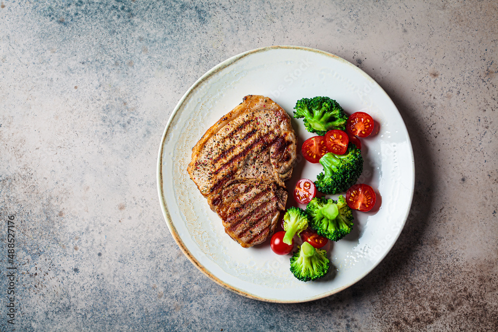 Canvas Prints grilled pork steak with broccoli and tomatoes on plate, dark background.