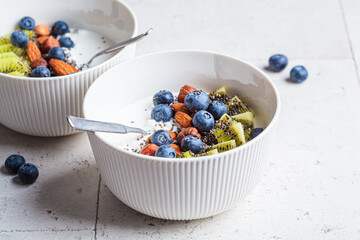 Breakfast cottage cheese with berries, nuts and chia seeds in white bowl.
