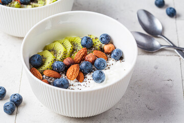 Breakfast cottage cheese with berries, nuts and chia seeds in white bowl.
