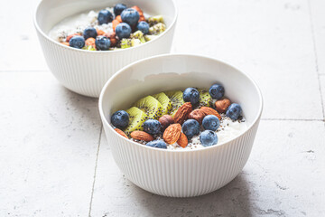 Breakfast cottage cheese with berries, nuts and chia seeds in white bowl.