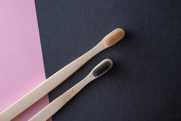 Two bamboo toothbrushes lie on a pink and black background. The concept of ecology, dental hygiene and health. Place for text. Copy paste. Close-up.