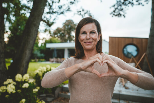 Smiling woman gesturing heart shape at backyard