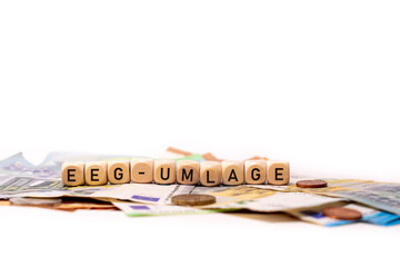German word for Renewable Energies Act, EEG-UMLAGE, spelled with wooden letters wooden cube on a plain white background with banknotes and coins, concept image