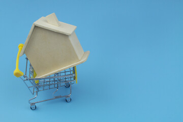 Buy and sell house and real estate concept, shopping cart with wooden house on blue background with copy space