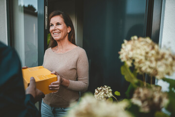 Happy woman receiving yellow package from delivery person at doorway