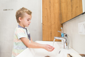 A five-year-old boy washes his hands in the bathroom. A boy of five years old, European outside...