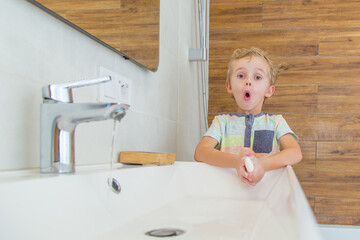 A five-year-old boy washes his hands in the bathroom. A boy of five years old, European outside washes his hands in the bathroom in front of the mirror