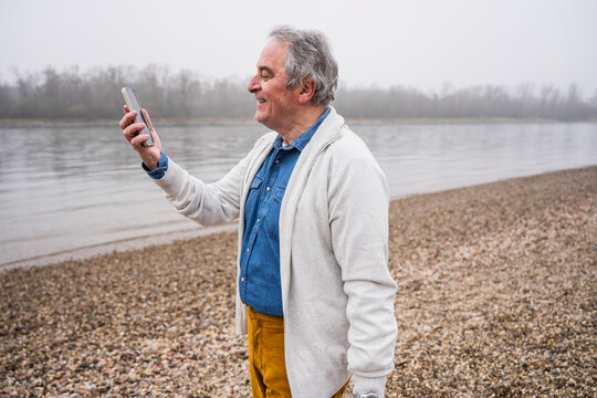 Smiling senior man doing video call through mobile phone at beach