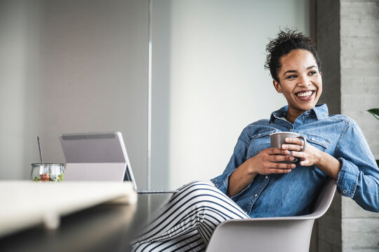 Happy businesswoman with coffee cup sitting on chair in office