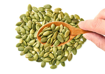 Hand holding wooden spoon filled with peeled pumpkin seeds. Close up, top shot, selective focus, white background. Healthy food concept