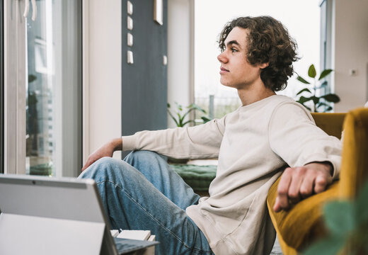 Thoughtful man sitting by sofa in living room at home