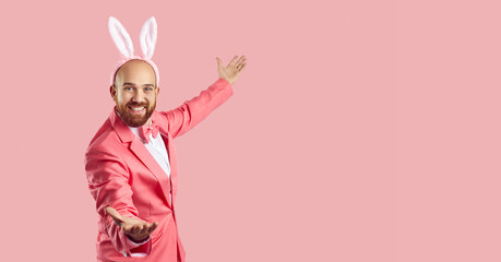 Funny man wearing bunny ears inviting you to Easter party. Happy young guy in pink suit and rabbit...