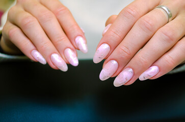 Close-up of beautiful female hands with a luxurious manicure, nails covered with pink gel polish with a design