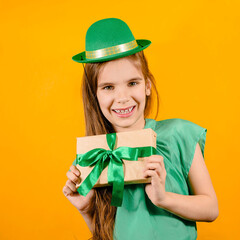 Cute girl child in a hat of a leprechaun for a St. Patrick's Day holds gift with green ribbon...