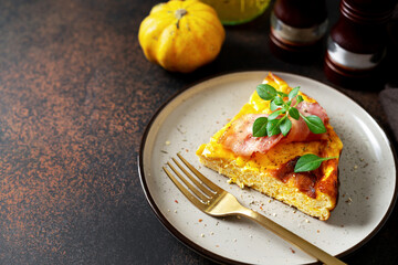 A piece of frittata with pumpkin, bacon and ricotta in a ceramic plate on a dark culinary background. Traditional Italian delicious homemade egg dish on the kitchen table