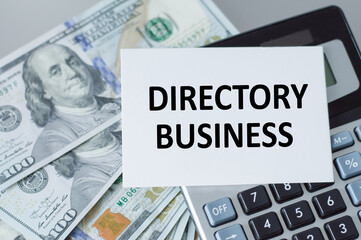 DIRECTORY BUSINESS text on a white card that sits on the calculator on the table next to the money dollars