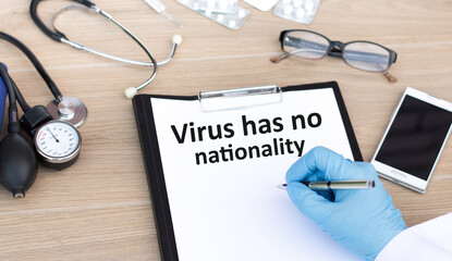 Doctor's hand writes text on white sheet Virus has no nationality