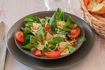 green salad with vegetables and parmesan shavings in a plate on a table