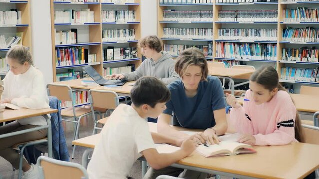 Schoolchildren studying in the school library write down a summary from a textbook in a exercise book, discussing topical issues. 
