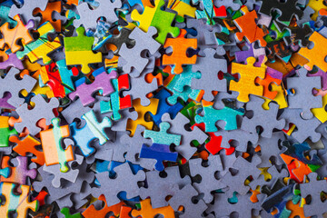Top view many jigsaw puzzle pieces over the entire frame. A background image of scattered colorful...