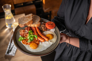 Traditional full English breakfast with fried eggs, sausages, beans, mushrooms, grilled tomatoes and bacon on hands