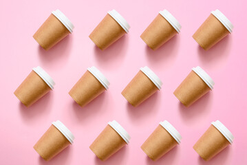 A lot of paper eco-friendly cups on a pink background. Pattern of disposable cups. The concept of using eco-friendly utensils for food delivery.