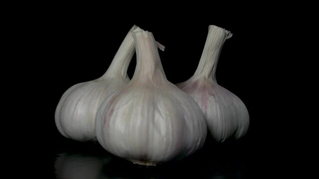 three heads of garlic rotate on a black background, close-up 
