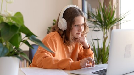 Teenage girl wears wireless headset greets teacher study online by skype, happy young woman learn language listen to lecture watch webinar on laptop, distance learning