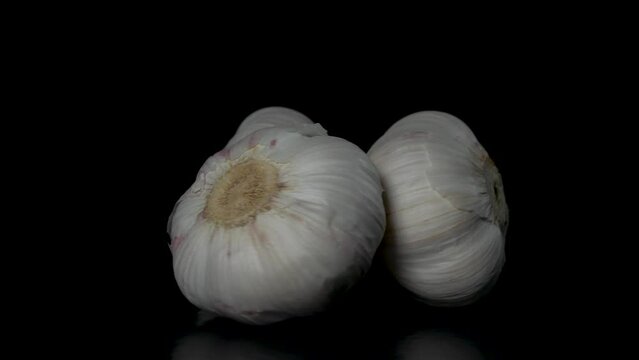 three heads of garlic rotate on a black background, close-up 