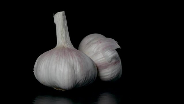 two heads of garlic rotate on a black background, close-up 
