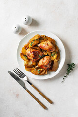 Baked chicken legs and potatoes with oranges, garlic and onions in a plate on a light culinary background