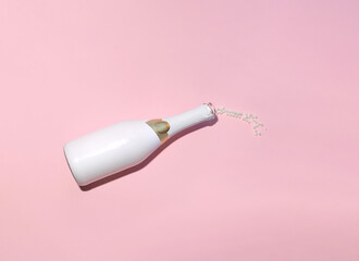 Champagne bottle and fine pearls, minimal creative arrangement against pastel pink background....