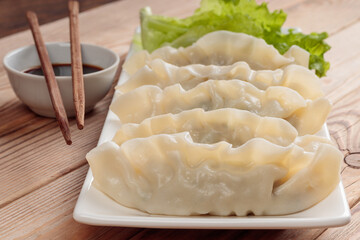 Close-up view of fresh boiled Chinese dumplings on rectangular plate with soy sauce and green salad on wooden background. Selective focus.