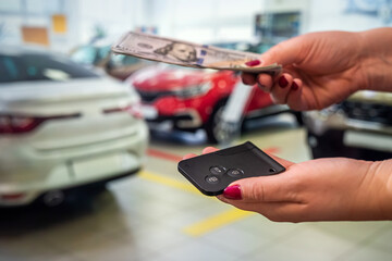 the new owner of the car holds a handful of dollars and car keys in the car showroom.