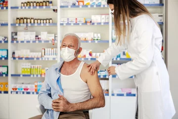 Papier Peint photo Pharmacie A nurse giving covid vaccine to an old man at pharmacy.