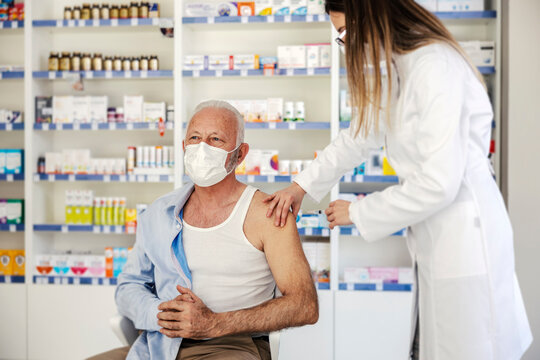 A nurse giving covid vaccine to an old man at pharmacy.