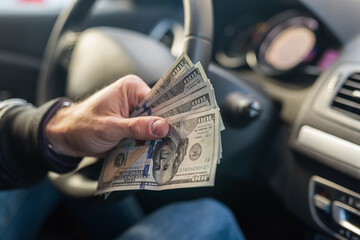 hands holding dollar bills in the middle in the car interior on the steering wheel background