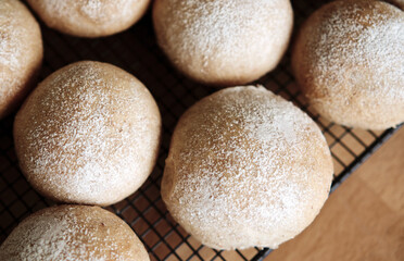 A top view looking down onto fresh homemade wholemeal bread buns cooling on a baking rack.