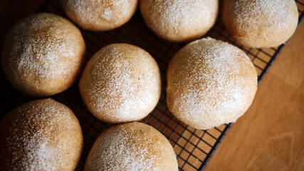 A top view looking down onto fresh homemade wholemeal bread buns cooling on a baking rack.