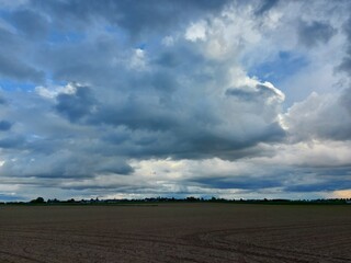 Bewölkter Himmel vor dem Sturm. Graue, schwere Wolken über dem Feld. Die Agrarlandschaft vor dem Sommerregen. Gepflügte Felder so weit das Auge reicht, bereit zur Aussaat. Eine ländliche Straße.