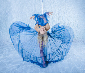 Poledens blonde with a beautiful figure, long legs, a dancer in a blue beautiful outfit sits beautifully and gracefully on a pylon