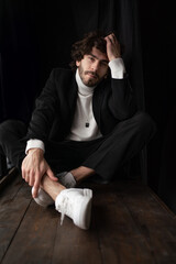 Obraz premium Young man with beard in white sweater and black suite against black background. High quality photo
