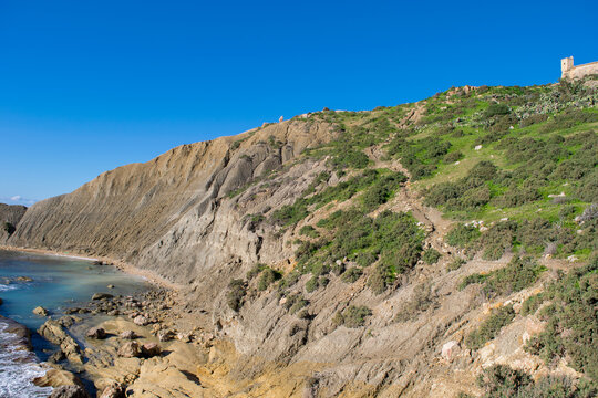 Steep blue clay slopes, with flaking debris forming scree on limestone along the coast of Xatt l-Ahmar, Ghajnsielem, Gozo, Malta, on a sunny day.