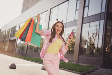 Portrait of beautiful cheerful wavy-haired girl buying things using gadget app bargain dancing...