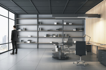 Young caucasian male looking out of window in modern office room interior. Future, tomorrow and executive concept.